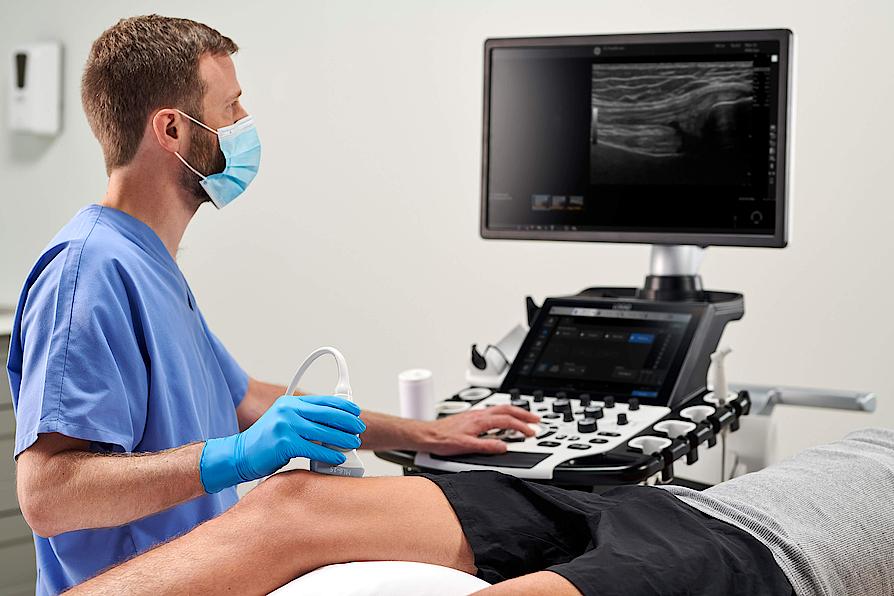 Imaginea prezintă un medic ce efectuează un examen ecografic MSK al genunchiului unui pacient.
