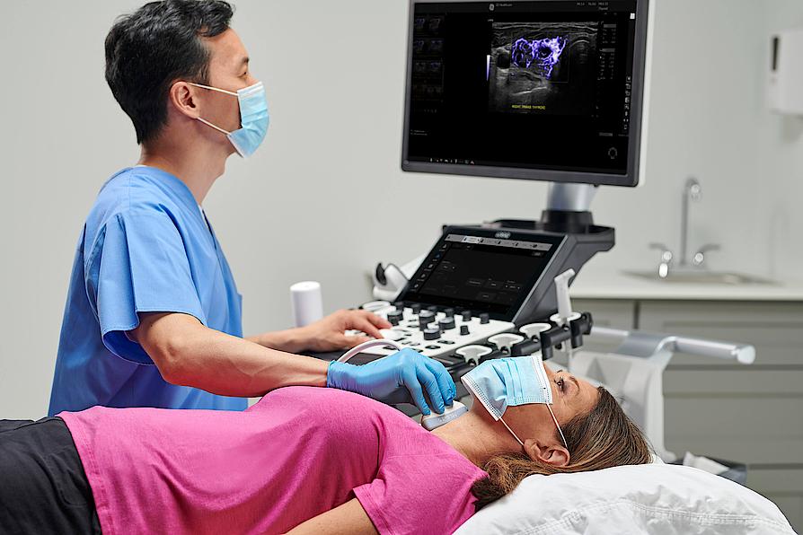 A képen egy orvos látható, aki pajzsmirigy-ultrahangvizsgálatot végez egy betegen.