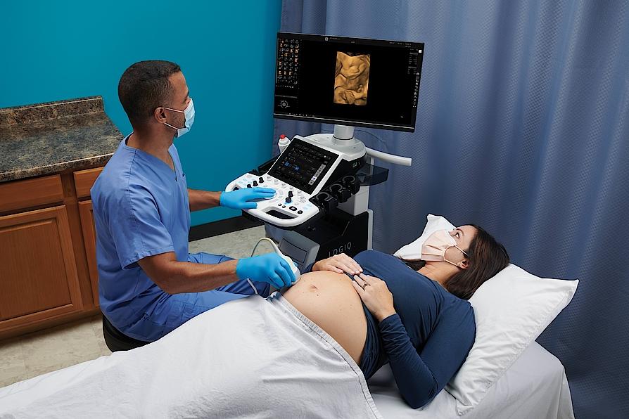 Imaginea prezintă un medic ce efectuează un examen ecografic al unei femei însărcinate.