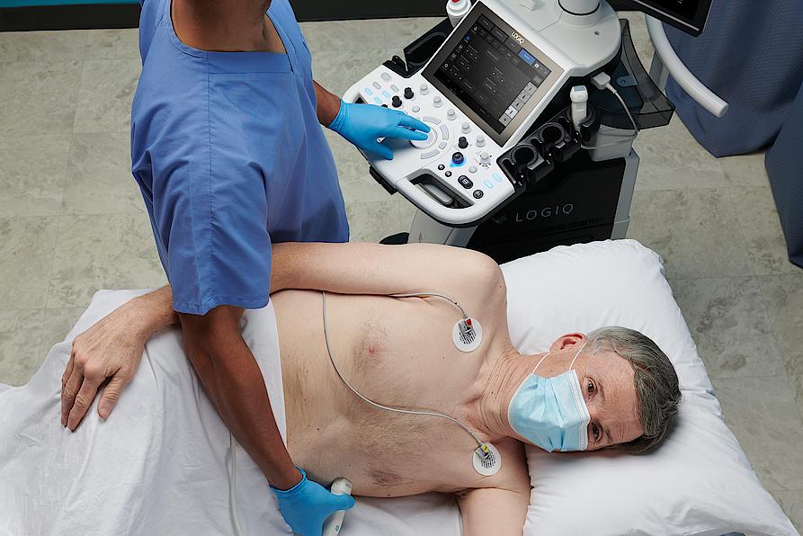 Imaginea prezintă un medic ce efectuează un examen ecografic cardiac al unui pacient.