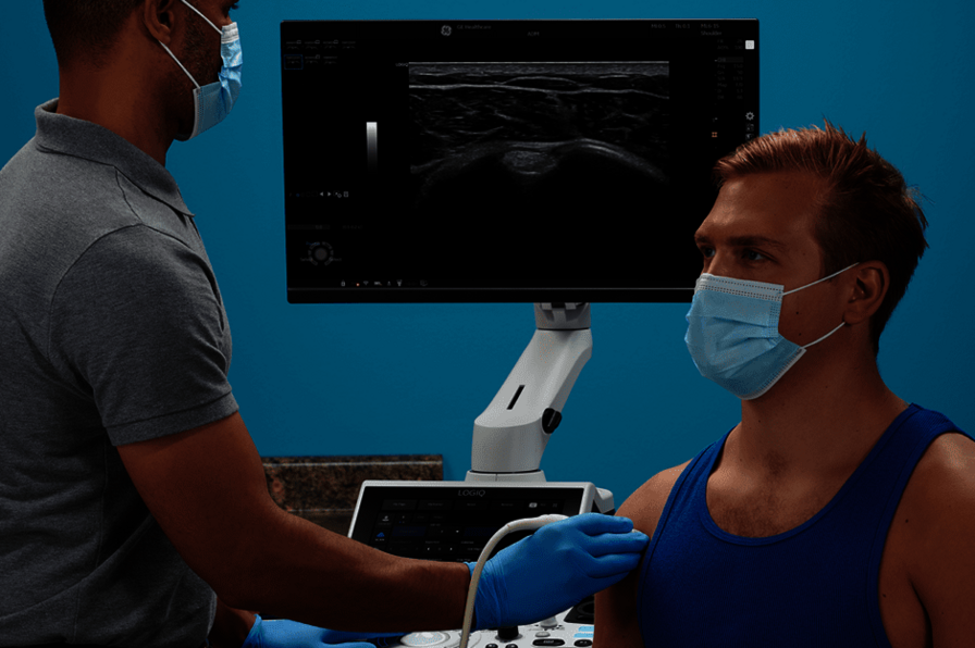 A képen egy orvos látható, aki mozgásszervi ultrahangvizsgálatot végez egy beteg vállán.